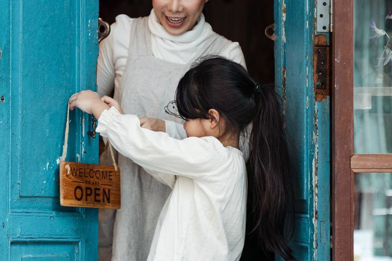 Mother and daughter hanging an open sign on their small shop door